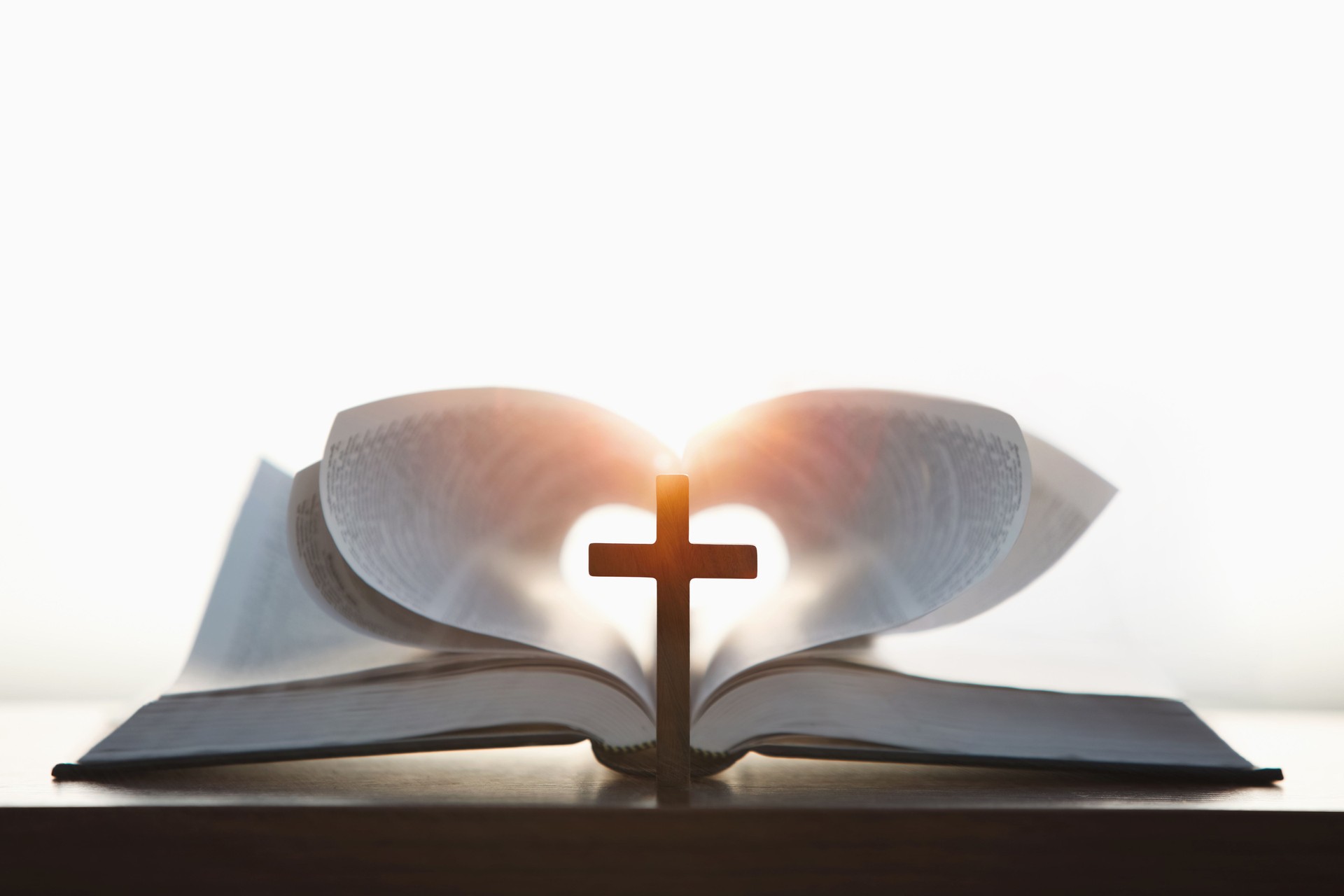 A cross symbolizing the death and resurrection of Jesus and a brightly lit heart-shaped Bible, the love of Jesus Christ in the background